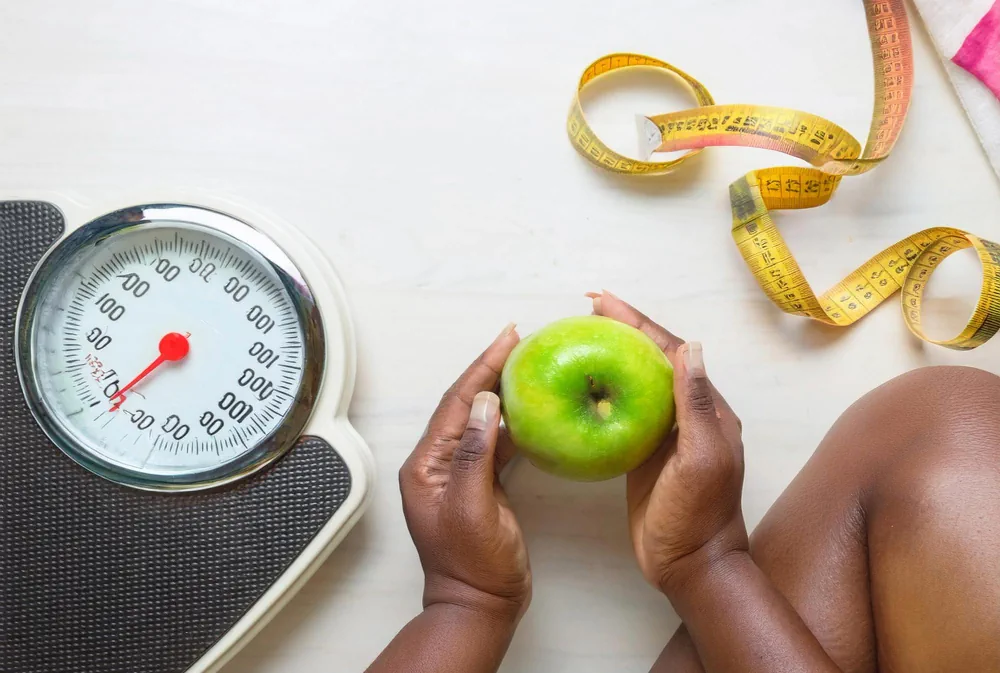 Weighing scale, apple, and measuring tape representing weight management and nutrition