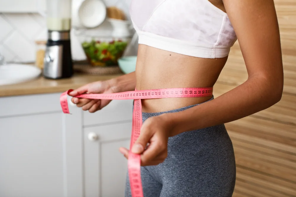 Woman measuring her waist at home while monitoring weight management progress